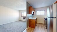 This single-floor unit offers a functional and straightforward layout designed for comfortable everyday living. The open-concept kitchen and living area form the heart of the space, where light hardwood-style flooring flows through the kitchen while plush carpet defines the living area. The kitchen is efficiently arranged in a galley style, featuring warm wood cabinetry, light countertops, a stainless steel refrigerator, a gas range, and a sink positioned beneath a window fitted with blinds that allows natural light to filter in. A wall-mounted heater and baseboard heating units are present throughout, ensuring consistent warmth.

The living area is generously proportioned, with neutral-toned walls, a textured ceiling, and windows that bring in natural light and outdoor views. Baseboard heaters line the walls, complementing the overall heating system.

The bedrooms are carpeted and bright, each featuring windows with blinds and baseboard heating, offering quiet, comfortable retreats. The bathroom is a clean, well-appointed space highlighted by a full soaking tub enclosed in white subway tile, a distinctive glass block window above, and a modern wood-accented vanity. The overall ambiance of the unit is clean, practical, and move-in ready.