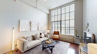 Located on North Broad Street in the heart of Philadelphia, this two-bedroom, one-bathroom residence offers a well-designed layout across a single floor. The living room is a standout space, boasting impressively tall ceilings and expansive floor-to-ceiling windows that flood the room with natural light and frame views of the surrounding cityscape. Rich hardwood flooring runs throughout the main living areas, adding warmth and continuity to the open feel.

The kitchen is fully equipped with stainless steel appliances, including a refrigerator, range, and built-in microwave, complemented by rich wood cabinetry, dark granite countertops, and tile flooring. A cozy dining nook adjacent to the kitchen provides a casual space for meals.

A carpeted hallway connects the bedrooms and bathroom, offering a quiet transition from the main living spaces. The primary bedroom is generously proportioned with soft carpeting, a dedicated closet, and window access for natural light. The bathroom features a wide vanity with stone countertops, rich wood cabinetry, a large mirror, and tile flooring. Two closets provide ample storage throughout. The overall ambiance is modern and urban, with clean lines and a neutral palette throughout.