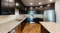 Located at 3730 Evergreen Dr in Monroeville, PA, this single-floor residence offers a well-designed layout with a blend of modern finishes and functional living spaces. The kitchen is a standout feature, showcasing rich dark cabinetry, light granite countertops, and a full suite of stainless steel appliances including a refrigerator, range, microwave, and dishwasher. Warm hardwood-style flooring runs throughout the main living areas, lending a cohesive and inviting feel. The open living area is bright and airy, with access to an outdoor door that brings in natural light and views of the surrounding greenery. Additional storage is conveniently located just off the kitchen. The bedroom is carpeted for comfort and includes a window that frames lush tree views, creating a peaceful atmosphere. The bathroom is thoughtfully finished with classic black-and-white penny tile flooring, dark vanity cabinetry with a white countertop, and a tub-shower combination with brushed gold fixtures. A large window in the bathroom allows natural light to fill the space. Overall, the residence presents a clean, neutral palette with quality finishes throughout, making it a comfortable and move-in-ready home.