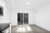 This single-floor unit showcases a clean, contemporary design characterized by an all-white palette, light hardwood-style flooring, and recessed lighting throughout. The galley-style kitchen is well-appointed with high-gloss white cabinetry extending to the ceiling, grey quartz countertops, a classic subway tile backsplash, and a full suite of stainless steel appliances, including a range, over-the-range microwave, dishwasher, and refrigerator. A undermount sink with a modern pull-down faucet completes the functional workspace.

The kitchen flows seamlessly into an open living area, which benefits from natural light streaming through large sliding glass doors that lead to a private balcony with a metal railing, offering views of the surrounding brick building exterior. The living space is bright and airy, with clean white walls and ample room for flexible furniture arrangements.

The bathroom maintains the unit's modern aesthetic, featuring light wood-style flooring, a white vanity with a dark countertop, recessed lighting, and a crisp, minimalist finish. Throughout the unit, the consistent use of neutral tones, modern hardware, and quality finishes creates a cohesive and polished living environment.