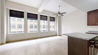 Located in the heart of Minneapolis at 730 Hennepin Ave, this one-bedroom, one-bathroom residence offers an efficient and thoughtfully laid-out single-floor plan. The open living area is brightened by a bank of large windows dressed with Roman shades, framing direct views of the surrounding downtown architecture. Polished terrazzo tile flooring runs consistently throughout the entire unit, lending a clean, urban character to the space. A ceiling fan adds both style and function to the main living area.

The kitchen is well-appointed with rich dark wood cabinetry, granite-style countertops, black appliances including a range, microwave, and refrigerator, and a central island that doubles as a breakfast bar — ideal for casual dining or meal prep.

The bedroom is a comfortable, well-proportioned room featuring the same terrazzo flooring and windows that overlook the city streetscape. A built-in closet with wire shelving provides organized storage.

The bathroom is finished with a dark wood vanity with a white countertop, a tub/shower combo with accessibility grab bars, and terrazzo flooring consistent with the rest of the unit. A drop ceiling with recessed lighting completes the space. This urban residence offers a practical and modern living experience in a prime downtown Minneapolis location.