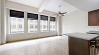 Located in the heart of Minneapolis at 730 Hennepin Ave, this one-bedroom, one-bathroom residence offers an efficient and thoughtfully laid-out single-floor plan. The open living area is brightened by a bank of large windows dressed with Roman shades, framing direct views of the surrounding downtown architecture. Polished terrazzo tile flooring runs consistently throughout the entire unit, lending a clean, urban character to the space. A ceiling fan adds both style and function to the main living area.

The kitchen is well-appointed with rich dark wood cabinetry, granite-style countertops, black appliances including a range, microwave, and refrigerator, and a central island that doubles as a breakfast bar — ideal for casual dining or meal prep.

The bedroom is a comfortable, well-proportioned room featuring the same terrazzo flooring and windows that overlook the city streetscape. A built-in closet with wire shelving provides organized storage.

The bathroom is finished with a dark wood vanity with a white countertop, a tub/shower combo with accessibility grab bars, and terrazzo flooring consistent with the rest of the unit. A drop ceiling with recessed lighting completes the space. This urban residence offers a practical and modern living experience in a prime downtown Minneapolis location.