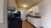 This single-floor residence offers a practical and comfortable layout across several well-defined living spaces. The galley-style kitchen is efficiently designed, featuring white cabinetry with ample upper and lower storage, dark countertops, and a suite of black appliances including a gas range, refrigerator, and dishwasher. Warm hardwood-style flooring runs throughout the kitchen, which connects conveniently to the rest of the unit via a central doorway.

The living area is generously sized, with plush neutral carpeting, a large window fitted with vertical blinds that invites natural light and outdoor views, and baseboard heating along the walls. The bedroom continues the same carpeted flooring and features a ceiling fan with integrated lighting, a wide horizontal window, and direct access to a closet and the hallway.

The bathrooms are clean and functional. One features a single-sink vanity with a light countertop, mirrored medicine cabinet, and tile flooring, while the other includes a full tiled tub-and-shower combination with classic white square tiles. Both bathrooms maintain a bright, neutral palette. Overall, the space presents a straightforward and livable layout with consistent finishes throughout.