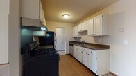 This single-floor residence offers a practical and comfortable layout across several well-defined living spaces. The galley-style kitchen is efficiently designed, featuring white cabinetry with ample upper and lower storage, dark countertops, and a suite of black appliances including a gas range, refrigerator, and dishwasher. Warm hardwood-style flooring runs throughout the kitchen, which connects conveniently to the rest of the unit via a central doorway.

The living area is generously sized, with plush neutral carpeting, a large window fitted with vertical blinds that invites natural light and outdoor views, and baseboard heating along the walls. The bedroom continues the same carpeted flooring and features a ceiling fan with integrated lighting, a wide horizontal window, and direct access to a closet and the hallway.

The bathrooms are clean and functional. One features a single-sink vanity with a light countertop, mirrored medicine cabinet, and tile flooring, while the other includes a full tiled tub-and-shower combination with classic white square tiles. Both bathrooms maintain a bright, neutral palette. Overall, the space presents a straightforward and livable layout with consistent finishes throughout.