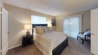This single-story residence offers a well-organized layout with distinct living, dining, kitchen, and sleeping areas, all finished in warm neutral tones that create a cohesive and welcoming atmosphere throughout.

The living room features soft carpeting, textured ceilings, and ample wall space for artwork, with warm lamp lighting contributing to a relaxed ambiance. It opens directly to the dining area, which is distinguished by a tray ceiling detail and a hanging chandelier. Wood-look flooring in the dining space adds contrast, and a window provides natural light. The adjacent kitchen is galley-style, featuring dark wood cabinetry, granite-tone countertops, a double sink, and black appliances, with wood-look flooring continuing underfoot.

The bedrooms are carpeted and well-proportioned. The primary bedroom includes sliding door access, generous closet space, and a connected en-suite bathroom. Additional bedrooms also offer closet space and natural light from windows. The bathrooms include dark vanity cabinetry with stone-tone countertops and wood-look flooring, maintaining a consistent design language with the rest of the home. Overall, the space presents a practical and comfortable living environment with consistent finishes throughout.