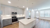 This single-story unit in Cypress, Texas, offers a well-designed open-concept layout that seamlessly connects the kitchen, dining, and living areas. The kitchen is a standout feature, equipped with gray shaker-style cabinetry extending to the ceiling for ample storage, bright white quartz countertops, and a full suite of stainless steel appliances including a range, over-the-range microwave, and refrigerator. A central island with an undermount sink and pendant lighting above serves as both a functional workspace and a casual gathering point. Wood-look flooring flows throughout the main living areas, complementing the clean, neutral color palette. The living area receives natural light through large windows and a glass-paneled door, and is outfitted with a ceiling fan. A conveniently tucked laundry closet houses a full-size washer and dryer. The bedroom features a ceiling fan, a bright window with outdoor views, and access to a generous walk-in closet with multi-tiered shelving and hanging rods. The full bathroom includes a dual-sink vanity with gray cabinetry, a wide framed mirror, and a tub-shower combination with subway tile surround, creating a clean and functional space throughout.