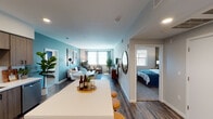 This well-designed single-floor residence combines modern aesthetics with functional living. The open-concept layout connects the kitchen, dining, and living areas seamlessly, creating a bright and inviting atmosphere enhanced by natural light from multiple windows. The kitchen is outfitted with stainless steel appliances including a gas range, microwave, and full-size refrigerator, complemented by wood-tone cabinetry, white quartz countertops, a classic subway tile backsplash, and a spacious island with bar seating. The living area features a striking teal accent wall, wood-look flooring, and a sitting nook with large windows that flood the space with natural light. The bedroom is a comfortable retreat with plush carpeting, a generous closet, and windows offering outdoor views. Two bathrooms serve the residence; one features a tub-shower combination and modern vanity, while the other offers a clean, minimalist design with coordinating finishes. Wood-look flooring runs consistently through the main living areas, tying together the cohesive contemporary design. Recessed lighting throughout adds warmth and functionality, making this a polished and move-in-ready living space.