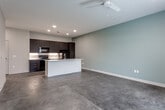 Located along I-29 N in North Kansas City, Missouri, this single-floor unit offers a clean, modern aesthetic throughout its well-designed layout. The open-concept kitchen and living area serves as the heart of the space, showcasing sleek dark cabinetry with brushed hardware, white quartz countertops, a white subway tile backsplash with under-cabinet lighting, and a full suite of black appliances including a range, microwave, dishwasher, and refrigerator. A central kitchen island with an integrated sink provides additional prep space and creates a natural gathering point. Large-format concrete-style tile flooring extends throughout the main living area, lending an industrial-modern character to the space. The generously sized living area offers an open canvas with neutral walls, recessed lighting, and ample room for flexible furniture arrangements. The bedroom features plush carpeting, a ceiling fan, and access to a spacious walk-in closet equipped with wire shelving on multiple walls for organized storage. A second carpeted bedroom benefits from a tall narrow window that brings in natural light and views of the surrounding greenery. The bathroom is finished with a white vanity, quartz countertop, undermount sink, large mirror, and a glass-enclosed shower, all set on light tile flooring.