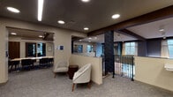 Located at 870 Toftrees Ave in State College, Pennsylvania, this thoughtfully designed single-floor amenity space offers a range of functional and social environments suited to residents and guests alike. The layout flows seamlessly from a central lounge area furnished with contemporary curved armchairs and a side table, set atop a geometric-patterned carpet that extends throughout the space. Exposed dark wood beam accents contrast with neutral cream walls, lending warmth and visual interest to the interiors.

A standout feature is the open dining and bar area, anchored by a substantial marble-topped counter with upholstered bar seating, pendant lighting overhead, and large windows that frame views of the surrounding wooded landscape. An adjacent kitchen or service area is partially visible beyond the counter, suggesting catering or dining support capabilities.

A dedicated conference room provides a professional setting with a rectangular table, ergonomic seating, a wall-mounted display screen, and glass-paneled private office or meeting rooms nearby. Directional signage and local map artwork add a community-oriented touch.

A lower-level area features a striking artistic accent wall composed of textured, multicolored panels in blues, grays, and creams, accompanied by casual round tables and bench seating. A railing overlook reveals access to an indoor pool area, rounding out this well-appointed facility.