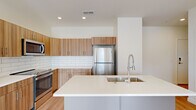 This well-appointed 2-bedroom, 2-bathroom residence offers a thoughtfully designed single-floor layout with contemporary finishes throughout. The open-concept kitchen and living area serves as the heart of the home, featuring warm wood-grain cabinetry, a crisp white subway tile backsplash, quartz countertops, and a full suite of stainless steel appliances including a range, microwave, and refrigerator. A large island with an undermount sink and a professional-style faucet provides additional prep space and a natural gathering point.

Light hardwood flooring flows through the main living areas, complementing the clean, neutral color palette. The spacious primary bedroom is bathed in natural light from multiple windows and a sliding glass door that opens directly to a private balcony with open urban skyline views. The second bedroom features plush carpeting and a large window framing bright outdoor views. A dedicated walk-in closet offers generous storage with full-perimeter hanging rods.

Both bathrooms are finished with wood-toned vanities, white quartz countertops, and brushed nickel fixtures. One bathroom includes a full soaking tub with shower combination. The overall design is clean, modern, and cohesive, creating a bright and functional living environment.