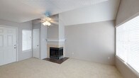This single-story space is designed with a neutral, light-filled palette throughout, creating a calm and cohesive atmosphere. The living area serves as a central gathering point, anchored by a tile-surround fireplace with a white mantel and accented by a vaulted ceiling section that adds visual depth. A ceiling fan overhead and plush carpeting underfoot contribute to the room's comfortable feel.

The kitchen features white cabinetry, granite-style countertops, and white appliances, including a refrigerator, range, and built-in microwave. A peninsula counter separates the kitchen from the adjoining carpeted dining or living area, which benefits from natural light streaming through a window. A half bath is conveniently accessible directly from this space.

The bedroom is generously proportioned, featuring soft carpet, a ceiling fan, a large window for natural light, and full-length mirrored sliding closet doors that enhance the sense of space. A glass-paned French door adds a refined architectural detail.

The full bathroom is finished with wood-look flooring, white cabinetry, granite-style countertops, a large vanity mirror, and a tub-shower combination, offering both function and clean, updated style.