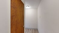 This single-floor, 2-bedroom, 1-bathroom unit offers a practical and well-organized layout across its compact footprint. Light wood-style luxury vinyl flooring runs consistently throughout the space, lending a clean and cohesive look to every room.

The kitchen is efficiently designed with warm wood cabinetry, granite-style countertops, a double-basin sink beneath a window that brings in natural light, and a stainless steel gas range — providing all the essentials for everyday cooking.

The spacious primary bedroom is notably generous in size, featuring dual windows that allow ample natural light to filter in, a ceiling fan with light fixture, and a baseboard radiator for heating. The second bedroom is similarly appointed with a ceiling fan and includes a built-in closet with shelving behind classic wood-toned bi-fold doors.

The bathroom showcases a retro aesthetic with pink ceramic wall tiles accented by a deep burgundy border, a decorative mosaic tile floor, a wall-mounted sink, and a grab bar — combining vintage character with functional detail.

Two hallways provide smooth transitions between rooms, and the unit's neutral white walls throughout create a bright, versatile canvas. The consistent flooring and clean finishes make this a straightforward and functional living space.