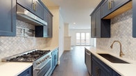 Located at 936 N High St in Columbus, Ohio's vibrant Short North arts district, this single-floor residence showcases thoughtfully designed interiors with a cohesive blend of modern finishes and classic detail. The galley-style kitchen is a standout feature, outfitted with rich navy-blue shaker cabinetry, brass hardware, quartz countertops, a decorative arabesque tile backsplash, and a professional-grade stainless steel gas range. The kitchen flows naturally into an open living area finished with wide-plank hardwood flooring, recessed lighting, and a striking white-trimmed fireplace that serves as the room's focal point. French doors at the far end of the living space invite natural light and provide access to the outdoors. The bedrooms are finished with plush wall-to-wall carpeting and feature five-panel interior doors with matte black hardware, along with generous closet space including a walk-in closet with built-in shelving and hanging rods. The bathroom is elegantly appointed with light wood-look tile flooring, a frameless glass walk-in shower with linear tile surround, a white quartz vanity, and a backlit mirror. Track lighting and recessed fixtures throughout ensure versatile illumination across the entire layout.