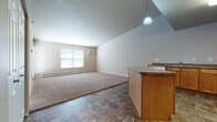This single-floor unit offers a practical and functional layout centered around an open-concept living and kitchen area. The kitchen is well-equipped with warm-toned wood cabinetry, granite-style countertops, a full suite of white appliances including a range, microwave, and refrigerator, and a central island that provides additional workspace and serves as a natural divider between the kitchen and living areas. Tile flooring runs throughout the kitchen and entry zones, transitioning to carpet in the living and bedroom spaces.

The living area is generously proportioned, featuring a sliding glass door with vertical blinds that brings in natural light. A wall-mounted air conditioning unit and baseboard heating provide year-round climate control. A pendant light fixture adds a subtle design accent above the kitchen island.

The bedroom is a comfortable, carpeted space with baseboard heating and a large closet with double panel doors. The full bathroom includes a single-sink vanity with matching wood cabinetry and granite-style countertop, a tiled floor, and a standard tub and shower combination unit. Overall, the space maintains a clean, neutral palette throughout.