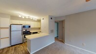 Located at 9991 Arbor Montgomery Ln in Cincinnati, Ohio, this single-floor residence offers a well-organized layout designed for comfortable everyday living. The kitchen is efficiently arranged with white cabinetry featuring wood-tone accents, stainless steel appliances including a refrigerator, range, and built-in microwave, along with a double sink and durable wood-look flooring. A peninsula counter connects the kitchen to the adjacent living area, creating an open, cohesive flow between spaces. The living area is carpeted and anchored by a tile-surround fireplace with a ceiling fan overhead, providing a warm and functional gathering space. Natural light filters in through windows with blinds, and a door provides direct outdoor access. A sliding glass door in another carpeted room opens to a balcony or patio, offering pleasant views of surrounding greenery. The bedroom is spacious with soft carpet, neutral gray walls, and connects to the rest of the unit through an interior hallway. The bathroom features a single-sink vanity with a large mirror, overhead lighting, a combined tub and shower, and wood-look flooring, rounding out the functional amenities of this well-appointed residence.