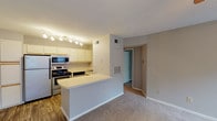 Located at 9991 Arbor Montgomery Ln in Cincinnati, Ohio, this single-floor residence offers a well-organized layout designed for comfortable everyday living. The kitchen is efficiently arranged with white cabinetry featuring wood-tone accents, stainless steel appliances including a refrigerator, range, and built-in microwave, along with a double sink and durable wood-look flooring. A peninsula counter connects the kitchen to the adjacent living area, creating an open, cohesive flow between spaces. The living area is carpeted and anchored by a tile-surround fireplace with a ceiling fan overhead, providing a warm and functional gathering space. Natural light filters in through windows with blinds, and a door provides direct outdoor access. A sliding glass door in another carpeted room opens to a balcony or patio, offering pleasant views of surrounding greenery. The bedroom is spacious with soft carpet, neutral gray walls, and connects to the rest of the unit through an interior hallway. The bathroom features a single-sink vanity with a large mirror, overhead lighting, a combined tub and shower, and wood-look flooring, rounding out the functional amenities of this well-appointed residence.