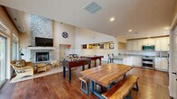 Located at 1298 Hartford Tpke in North Haven, Connecticut, this single-floor combined kitchen and living room offers a warm, well-appointed layout designed for both comfort and functionality. Rich hardwood flooring flows throughout the entire space, tying together the open-concept design seamlessly.

The living area is anchored by a striking floor-to-ceiling stone fireplace, which serves as a dramatic focal point beneath soaring vaulted ceilings. Large sliding glass doors flood the space with natural light while providing direct access to an outdoor patio area, offering pleasant views of the surrounding greenery.

The kitchen is thoughtfully outfitted with cream-toned cabinetry featuring detailed millwork, granite countertops, stainless steel appliances including a double oven range and built-in microwave, and a double sink beneath a bright window. A kitchen island with a granite surface doubles as a breakfast bar with bar stool seating, creating a natural transition between the kitchen and the living area. Wainscoting details along the lower walls add a classic, refined touch throughout the space.

Recessed lighting complements the abundant natural light, ensuring the space remains bright and inviting at all hours. The overall ambiance is cozy yet open, blending traditional architectural details with modern amenities in a cohesive, functional design.
