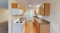 This single-floor unit is thoughtfully laid out to maximize functionality across its living areas. The spacious main living area is finished with neutral-toned carpet and features large windows that admit generous natural light, offering views of surrounding greenery. A wall-mounted air conditioning unit and baseboard heaters provide year-round climate control. The room opens toward a connecting hallway, creating a smooth flow throughout the unit.

The galley-style kitchen is outfitted with light wood cabinetry on both sides, offering ample upper and lower storage. Dark laminate countertops provide workspace alongside a stainless sink, and white appliances including an electric range, refrigerator, and over-the-range microwave complete the setup. Light hardwood-style flooring runs through the kitchen, transitioning to carpet in adjacent rooms.

The bedrooms are carpeted and finished with the same warm neutral palette seen throughout. Each room benefits from natural light via individual windows, and baseboard heaters maintain comfort. At least one bedroom includes a wide reach-in closet with a built-in shelf and hanging rod. The overall ambiance is clean, practical, and move-in ready.