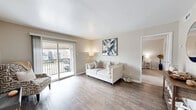 Located in Seabrook, Texas, this single-story, one-bedroom, one-bathroom residence offers a thoughtfully designed layout across a compact yet functional floor plan. The bright living room serves as the heart of the home, featuring wood-style flooring, neutral warm-toned walls, and a textured ceiling. Large sliding glass doors open to a private balcony, flooding the space with natural light and providing outdoor views of the surrounding community. The living area flows naturally into a dedicated dining room, which features a window with blinds and ample space for a full dining table. The galley-style kitchen is efficiently organized with gray cabinetry on both sides, light quartz countertops, a tile backsplash, stainless steel sink, and black appliances including a range and refrigerator. The bedroom is carpeted and generously sized, equipped with a ceiling fan and a window that brings in natural light. It connects to a spacious walk-in closet with a full-length hanging rod and built-in shelving. The bathroom includes a combined tub and shower with tile surround, gray vanity cabinetry, and quartz countertops. Wood-style flooring carries throughout the main living areas, tying the space together with a clean, cohesive aesthetic.