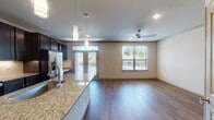 This single-floor residence offers a thoughtfully designed open-concept layout that seamlessly connects the kitchen and living areas. The kitchen is a standout feature, equipped with rich dark-wood cabinetry extending to the ceiling, granite countertops, a large center island, stainless steel appliances including a French door refrigerator, electric range, and over-the-range microwave, complemented by a classic subway tile backsplash. A built-in desk area adds functional workspace within the kitchen. Warm hardwood-style flooring flows throughout the main living areas, while recessed lighting and elegant pendant fixtures illuminate the space. The living area benefits from multiple windows and glass French doors that invite natural light and provide outdoor views. The bedroom features plush carpet, a ceiling fan, and a generous window with exterior views. The primary bathroom is well-appointed with a dual-sink granite vanity, dark cabinetry, a walk-in shower, a soaking tub with tile surround, and framed mirrors. A spacious walk-in closet with extensive built-in shelving and hanging systems provides ample storage. Crown molding accents add a refined finish throughout the home.