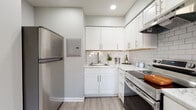 This single-floor residence offers a thoughtfully designed layout that balances comfort and functionality. The kitchen stands out as a highlight of the space, featuring crisp white shaker-style cabinetry, light-toned countertops, a classic white subway tile backsplash, stainless steel appliances including a full-size refrigerator, and durable wood-look flooring. The clean, bright aesthetic creates an inviting environment for cooking and entertaining.

The bedrooms are finished with soft wall-to-wall carpeting in neutral tones and painted in a calming grey palette. Each room offers generous closet storage, with bifold closet doors providing easy access. Natural light filters in through windows fitted with horizontal blinds, offering views of the surrounding greenery.

The bathrooms echo the home's modern aesthetic, featuring white subway tile surrounds, white vanities with under-sink storage, brushed nickel fixtures, frameless mirrors, and wood-look tile flooring that adds warmth to the space. The overall design maintains a cohesive, clean look throughout.

The floor plan, as seen in the dollhouse view, reveals a practical and well-organized layout with a dining area and multiple bedrooms arranged for privacy and ease of flow, making this a comfortable and move-in ready space.