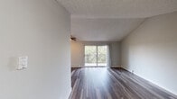 This single-floor residence offers a thoughtfully designed layout that balances open living spaces with functional private areas. The main living room is bright and spacious, featuring dark-toned laminate hardwood flooring, a textured ceiling, a ceiling fan, and a sliding glass door that opens onto a private balcony overlooking lush tree canopy — allowing natural light to flood the interior. Baseboard heating runs along the perimeter, ensuring year-round comfort.

The kitchen has been updated with crisp white shaker-style cabinetry, grey quartz countertops, a classic white subway tile backsplash, and a full suite of stainless steel appliances including a refrigerator, electric range, over-the-range microwave, and dishwasher. Light hardwood-style flooring complements the clean, modern aesthetic.

The bathroom is equally refined, showcasing a white vanity with grey countertop, an undermount sink with brushed nickel fixtures, a framed mirror, elegant pendant-style vanity lighting, and built-in cabinetry for additional storage. Dark hardwood flooring continues throughout.

The bedroom area is carpeted for comfort and includes a well-organized closet system with shelving and hanging rods. A connecting hallway provides a smooth flow between all areas of the home, creating a cohesive and livable layout throughout.