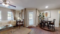 This single-story residence offers a thoughtfully designed layout with warm, neutral tones and classic finishes throughout. The living room features rich hardwood-style flooring, crown molding, a ceiling fan, and generous natural light provided by windows dressed with layered curtains and blinds. A glass-top coffee table, patterned area rug, and eclectic accents give the space a stylish character.

Adjacent to the living area, the dining space accommodates a round table with seating for several guests and benefits from direct outdoor access via a glass-paneled door, enhancing the sense of connection to the exterior.

The galley-style kitchen is efficiently organized, featuring warm wood cabinetry, dark granite-style countertops, hardwood-style flooring, and black appliances including a gas range, dishwasher, and refrigerator.

The bedroom is a serene retreat with plush carpet, crown molding, a ceiling fan, and a distinctive decorative headboard composed of silver circular mirrors. A window with sheer curtains allows natural light to filter softly into the room, and a walk-in closet is accessible nearby.

The bathroom includes a tub-shower combination with white tile surround, wood cabinetry with overhead storage, and a vanity with a mirror. The space is clean and functional, maintaining the home's consistent warm aesthetic.