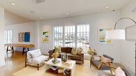 Located at 406 Ledbury Rd in Wilmington, NC, this thoughtfully designed single-floor amenity space offers a generous and well-appointed layout across a substantial footprint. The interior is bathed in natural light throughout, thanks to large multi-pane windows that frame views of the surrounding community and outdoor pool area.

The two living rooms each carry a distinct character. One features a dramatic vaulted ceiling, a bold teal accent wall with board-and-batten detailing, a wall-mounted TV, and oversized pendant lighting — creating a stylish, lounge-like atmosphere. The other is bright and airy, furnished with mid-century modern seating and colorful wall art, with wide windows offering neighborhood views.

The two dining areas are equally inviting, with grid-pane windows flooding each with natural light. One dining space includes a warm wood table with upholstered seating and a gold-toned sideboard, creating an elegant yet relaxed setting.

The fitness center is a standout feature, boasting soaring vaulted ceilings, clerestory windows, ceiling fans, and dramatic pendant lighting. It is fully equipped with cardio machines, strength equipment, free weights, and cable systems.

A dedicated business lounge offers a long wood work surface, desktop computers, and a striking herringbone-patterned teal accent wall with Edison-bulb sconces. The hallway entry area is polished with concrete flooring and sophisticated furnishings, seamlessly connecting all spaces.