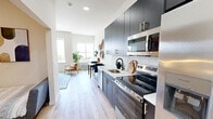 Located at 169 North Main Street in Port Chester, NY, this thoughtfully designed one-bedroom, one-bathroom unit maximizes every square foot with a modern, efficient layout. The entry hallway leads into a galley-style kitchen outfitted with slate-blue cabinetry, gold hardware accents, a white tile backsplash, stainless steel appliances — including a built-in microwave, electric range, and refrigerator — and a white quartz countertop with an undermount sink. Light wood-style flooring runs throughout, creating a seamless flow into the combined dining and living areas. The dining space features a large window that frames outdoor views and fills the room with natural light, while the living room offers generous wall height and additional windows that enhance the bright, airy ambiance. The bedroom is a cozy, well-appointed retreat with a closet, wood flooring, and tall ceilings. The bathroom is finished with large-format floor tiles, a backlit vanity mirror, a white quartz countertop, and a tiled walk-in shower. Two closets, a dedicated laundry area, and a utility room round out the functional amenities of this well-appointed unit.