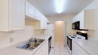 Located at 410 Jason Dr B11 in Richmond, Kentucky, this single-floor unit offers a practical and well-organized layout suited for comfortable everyday living. The galley-style kitchen is outfitted with white cabinetry, light countertops, a double stainless steel sink, and a full suite of appliances including an electric range, dishwasher, microwave, and refrigerator. Light tile flooring runs throughout the kitchen, creating a clean and easy-to-maintain surface. The living area features plush carpeting, a ceiling fan with integrated lighting, and access to natural light through a pair of windows and a glass-paned exterior door, providing a bright and airy feel. The bedroom is generously proportioned with soft carpet, multiple windows that invite natural light, and a notable walk-in closet with built-in shelving, offering ample storage space. The bathroom is finished with tile flooring, a single vanity with a large mirror, and a tub and shower combination with tiled surround. Neutral warm tones are carried consistently throughout the unit, lending the space a cohesive and inviting atmosphere. The overall layout, as seen in the dollhouse view, flows efficiently from the main living area through to the kitchen and private quarters.