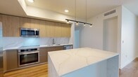 Located along Tampa's iconic Riverwalk Trail in the heart of downtown (33602), this contemporary 2-bedroom, 2-bathroom residence offers a thoughtfully designed single-floor layout with high-end finishes throughout. The open-concept kitchen is a standout feature, showcasing warm wood cabinetry, a striking marble-veined quartz island and backsplash, stainless steel appliances including a French door refrigerator, built-in oven, induction cooktop, microwave, and dishwasher, all set above light hardwood flooring. A sleek pendant light rail adds an industrial-modern touch above the island. The living areas continue the hardwood flooring and are bathed in natural light, with floor-to-ceiling sliding glass doors leading to a private balcony that offers sweeping elevated views of the Tampa skyline and surrounding cityscape. The generously sized primary bedroom features plush carpeting and large windows that frame the panoramic views. The primary bathroom is appointed with a glass-enclosed walk-in shower and a separate soaking tub, both finished in elegant marble-style tile. The second bathroom mirrors the same refined aesthetic with a tub/shower combo and marble tile surround. Two closets and two hallways provide practical storage throughout this well-appointed urban residence.