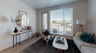 This single-floor residence showcases a thoughtfully designed open-concept layout with light wood-style flooring flowing throughout the main living areas. The kitchen serves as a focal point, featuring a large center island with a dark quartz countertop and bar seating, contrasting dark lower cabinetry paired with crisp white upper cabinets, and a full suite of stainless steel appliances including a refrigerator, range, microwave, and dishwasher. Recessed lighting illuminates the space efficiently.

The living area is generously sized, anchored by large windows fitted with horizontal blinds that admit abundant natural light. A glass-paned door opens directly onto a private balcony, offering outdoor views of the surrounding area. The space comfortably accommodates both a seating and dining arrangement.

Two bedrooms feature plush carpeting, ample closet space, and windows that bring in natural light. One bedroom includes a walk-in closet, while both provide a calm, comfortable retreat. The bathroom is cleanly finished with a full soaking tub and shower combination, wood-style flooring, and a dark-toned vanity. Throughout, the neutral color palette and modern detailing create a cohesive, contemporary ambiance.