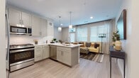 This well-appointed single-floor residence offers a thoughtfully designed open-concept layout that seamlessly connects the kitchen, dining, and living areas. The kitchen is a standout feature, showcasing soft sage-toned shaker-style cabinetry, crisp white quartz countertops, a central island with an undermount sink, and a full suite of stainless steel appliances including a gas range, over-the-range microwave, dishwasher, and French door refrigerator. Pendant lighting above the island adds a refined touch, while light wood-look flooring flows throughout the main living areas.

The open living space is bathed in natural light from a bank of large windows fitted with blinds and sheer curtains, creating a bright and welcoming atmosphere. Two well-sized bedrooms offer comfortable retreats, each with natural light from generously sized windows. The primary bedroom features a rich wood-toned headboard and warm, layered textiles. A secondary bedroom includes a stylish wall-mounted open shelving unit.

Two full bathrooms are finished with white cabinetry, quartz countertops, undermount sinks, and light wood-look tile flooring. One bathroom includes a soaking tub with tiled surround, while the other features a single-vanity design. The overall aesthetic is modern, clean, and cohesive throughout.