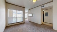 This single-story, one-bedroom, one-bathroom residence offers a thoughtfully designed layout that balances open living space with practical functionality. The main living area is generously sized, featuring plush wall-to-wall carpeting, crown molding, and a ceiling fan overhead. Large windows fitted with blinds allow ample natural light to fill the room while providing views of the surrounding exterior. The open flow of the space is enhanced by vaulted-style ceilings that lend an airy, spacious feel throughout.

The kitchen is positioned adjacent to the living area and features warm wood cabinetry, a breakfast bar pass-through that connects to the main living space, and hardwood-style flooring. Black appliances, including a refrigerator and range, are included, and the layout allows for easy sightlines into the living and dining areas.

The bedroom is a comfortable retreat, also carpeted, with a ceiling fan, crown molding, and ample wall space. It connects conveniently to the bathroom, which includes a long vanity topped with granite-style countertops, dark wood cabinetry, dual mirrors, and tile flooring. An in-unit washer and dryer closet with louvered doors adds practical convenience. The unit also provides direct access to an outdoor balcony or patio through a glass-paned door in the living area.