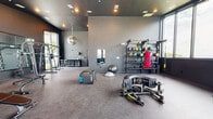 Located at 1200 Foster St NW in Atlanta, GA, this fitness center offers a generously sized, single-floor workout space designed for a comprehensive exercise experience. The interior features a sleek, modern aesthetic with dark gray walls, rubber flooring, and recessed lighting complemented by ceiling fans that maintain airflow throughout the space.

Large floor-to-ceiling windows line the perimeter, flooding the gym with abundant natural light and offering open views of the surrounding Atlanta skyline and greenery. The high ceilings add a sense of openness, and a distinctive mirrored disco ball serves as a unique decorative focal point near the entrance.

The fitness floor is thoughtfully arranged to accommodate a wide variety of training disciplines. Cardio equipment includes multiple treadmills, stationary bikes, and a stair climber, all positioned along the windowed walls to maximize the outdoor views during workouts. The strength training area features a cable machine, a dumbbell rack, weight benches, and a squat rack. Functional training tools such as medicine balls, kettlebells, a punching bag, TRX suspension trainers, plyo boxes, a heavy-duty tire, and a rowing-style sled machine further enhance the versatility of the space. Wall-mounted mirrors expand the sense of depth throughout the room, making it feel even more expansive and dynamic.