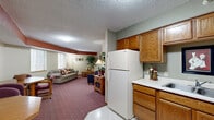 Located at 1480 Park St in White Bear Lake, MN, this single-floor studio-style unit offers a thoughtfully organized layout that maximizes every square foot of its compact footprint. The open-plan living and dining area is anchored by plush, patterned carpeting in warm burgundy tones, creating a cozy and inviting atmosphere. A textured ceiling runs throughout, while a distinctive terracotta-toned architectural beam adds visual character to the living space. Multiple windows fitted with horizontal blinds allow natural light to filter in and offer views of the surrounding wooded scenery, enhancing the sense of openness.

The kitchen is efficiently designed with warm oak cabinetry providing ample upper and lower storage, white laminate countertops, a double-basin sink, and a full suite of white appliances including a refrigerator, electric range, and microwave. Light vinyl flooring in the kitchen transitions seamlessly into the carpeted living and dining zones. A dedicated dining area accommodates a round table and chairs, making the space well-suited for everyday living. The unit's entry door is conveniently positioned adjacent to the kitchen area, with a coat hook strip offering practical storage just inside the entrance. Overall, the unit presents a functional, well-appointed living environment.