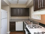 River City Place is a single-story residence designed with a practical and comfortable layout. The interior is finished with a neutral warm-beige color palette throughout, creating a cohesive and inviting atmosphere across all rooms.

The kitchen is efficiently designed and features rich dark-wood cabinetry, granite-style countertops, and a peninsula with additional counter space. It is equipped with a gas range, dishwasher, and refrigerator, all set atop durable hardwood-style flooring. A window above the sink allows for natural light to fill the space.

The living area transitions seamlessly from the kitchen and features plush wall-to-wall carpeting alongside hardwood-style flooring, offering a versatile and comfortable space. Multiple bedrooms are carpeted and bathed in natural light through horizontal-blind-covered windows. Each room features clean white baseboards and textured ceilings, maintaining a consistent design throughout.

The bathroom is well-appointed with a full tub-shower combination, a toilet, and a vanity topped with a granite-style countertop and a round mirror framed by a multi-bulb light fixture. Hardwood-style flooring completes the look, tying it to the rest of the home.

Overall, River City Place offers a clean, move-in-ready environment with functional features and a warm, understated aesthetic.