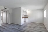 Located at 2811 Central Ave in Fort Myers, Florida, Unit 311 is a well-maintained single-floor residence featuring a bright, neutral palette and light wood-look flooring throughout. The open living area is generously proportioned, offering a clean and versatile space with smooth white ceilings and a calm, airy ambiance. A pass-through opening connects the living area to the kitchen, enhancing the sense of openness while maintaining defined functionality. The kitchen is thoughtfully appointed with white cabinetry, warm brown stone-look countertops, a double-basin stainless steel sink, and black appliances including a range and refrigerator — all set against the same light flooring that runs throughout the unit. A hallway leads to the bedroom, which features a large window that frames views of lush tropical greenery, allowing natural light to fill the room. A closet with sliding doors provides ample storage. The bathroom is finished with clean, simple lines, featuring a full soaking tub with shower surround, a toilet, and matching wood-look flooring. The overall design of the unit is understated and functional, offering a comfortable living environment in a convenient Fort Myers location.