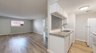 Located on Audley Street in Houston, TX, this single-story unit presents a clean, updated interior with a cohesive neutral palette throughout. Light wood-look plank flooring extends across all living areas, complementing the soft gray walls and bright white trim to create a fresh, modern aesthetic.

The open-concept living area is generously proportioned, allowing natural light to filter in through multiple windows fitted with horizontal blinds. A pass-through peninsula connects the living space to the galley-style kitchen, which features granite-look countertops, white shaker-style cabinetry, a subway tile backsplash, and white appliances including a range and refrigerator. Ample upper and lower cabinet storage lines both sides of the kitchen corridor.

The bedrooms offer comfortable dimensions, with one room featuring a ceiling fan with light fixture and a wide window. Additional rooms maintain the same wood-look flooring and neutral tones, providing versatile living spaces.

The bathroom is finished with large-format wood-grain ceramic tile covering the full tub surround, accented by a decorative mosaic border strip and a handheld showerhead, lending a polished, contemporary feel to the space.