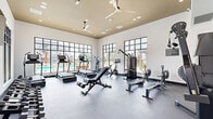 Located at 4542 Gender Rd in Columbus, Ohio, this well-appointed fitness center offers a thoughtfully designed single-floor layout for a comprehensive workout experience. The space is characterized by soaring ceilings with a distinctive gold-toned upper accent panel, recessed lighting, and dual ceiling fans that ensure optimal air circulation throughout.

Floor-to-ceiling, black-framed grid windows line multiple walls, flooding the interior with abundant natural light and providing unobstructed views of an outdoor pool area and the surrounding community. The open, airy atmosphere is further enhanced by clean white walls and durable dark rubber flooring suited for high-intensity use.

The fitness floor is fully equipped with a diverse range of cardio and strength training equipment. Cardio offerings include Freemotion treadmills and incline trainers, a stationary cycle, and a rowing machine. Strength training is supported by a multi-function cable machine, an adjustable weight bench, and a well-stocked dumbbell rack. Wall-mounted mirrors along one side of the room amplify the sense of space and allow users to monitor their form. The overall design strikes a balance between functionality and modern aesthetics, creating an inviting environment for all fitness levels.