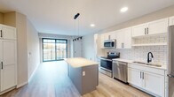 Located in Eau Claire, WI, this contemporary single-floor residence showcases a clean, modern design with light luxury vinyl plank flooring throughout. The open-concept kitchen is a standout feature, equipped with white shaker cabinetry accented by matte black hardware, a classic white subway tile backsplash, stainless steel appliances including a range, microwave, dishwasher, and refrigerator, and a central gray island with a light quartz countertop. Pendant lighting with industrial-style black fixtures illuminates the kitchen and flows into the adjoining living area, which opens to a private balcony through large, grid-paned windows that bring in generous natural light. A stacked washer and dryer unit is conveniently integrated into the main living space. The unit includes two full bathrooms: one featuring a walk-in shower with sliding glass doors framed in matte black, and the other a full soaking tub/shower combo, both equipped with accessibility grab bars and white vanities. The bedrooms are bright and well-proportioned, each with large windows offering outdoor views of the surrounding Eau Claire landscape. Recessed lighting and a neutral color palette throughout lend the space a fresh, move-in-ready appeal.