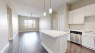 Located in Dallas, TX 75219, this well-appointed 2-bedroom, 3-bathroom residence offers a thoughtfully designed single-level layout with modern finishes and a neutral color palette throughout. The open-concept kitchen and living area serves as the heart of the home, anchored by a large central island with white quartz countertops, ample cabinetry, a textured tile backsplash, and a full suite of stainless steel appliances including a refrigerator, range, and dishwasher. Pendant lighting over the island adds a polished touch, while rich dark hardwood flooring flows seamlessly into the spacious living area, which features a ceiling fan and a window that invites natural light. The primary bedroom is generously sized and connects to its own bathroom. The second bedroom is carpeted and benefits from dual windows providing bright, natural light. A flexible den space adds versatility for a home office or additional living area. Three full bathrooms are finished with white subway tile, soaking tubs, and clean white vanities with quartz countertops. Additional highlights include three closets, a dedicated laundry room, and two hallways connecting the well-organized floor plan for easy flow and functionality.
