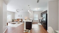 Located at 5776 Thomaston Rd in Macon, GA, this single-story residence offers a thoughtfully designed open-concept layout that seamlessly connects the kitchen, dining, and living areas. The kitchen is a standout feature, equipped with dark espresso cabinetry, black appliances, a sleek white quartz peninsula with bar seating, and stylish pendant lighting overhead. Hardwood-style flooring runs throughout the main living areas, complementing the neutral, light gray tones on the walls. The dining area is distinguished by an elegant wainscoting accent wall and a contemporary pendant light fixture, adding a refined architectural detail to the space. The living room benefits from natural light streaming through windows fitted with blinds, and is further enhanced by a ceiling fan. The bedroom is carpeted and features multiple windows that invite ample sunlight, along with a ceiling fan and a dedicated closet. The bathroom includes a soaking tub with a shower curtain and built-in wall shelving for storage. Additional conveniences include an in-unit laundry area and a closet. Throughout, the residence maintains a cohesive, modern aesthetic with clean lines and a bright, airy ambiance.