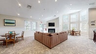Located at 15 Iron Horse Dr in Bedford, NH, this single-story clubhouse facility offers a well-rounded collection of amenity spaces designed for comfort, productivity, and wellness. The welcoming entrance hallway features vaulted ceilings, wainscoting, plush carpeting, and curated artwork, setting an inviting tone throughout. The spacious lounge area serves as the heart of the facility, centered around a gas fireplace with a classic white mantel and a wall-mounted flat-screen TV above. A large sectional sofa anchors the room, which is bathed in natural light from multiple windows. A glass door provides direct access to an outdoor patio area. The conference and meeting room offers a clean, modern aesthetic with a drop ceiling, patterned carpet tile flooring, large windows, and a generous rectangular table with ample seating — ideal for gatherings or presentations. The fully equipped fitness center is generously sized, featuring rubber flooring, full-length mirrors, and a comprehensive array of cardio machines and strength-training equipment. The kitchen area includes stainless steel appliances, white cabinetry, and tile flooring, providing functional support for events. Together, these spaces deliver a cohesive and well-appointed community facility.