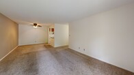 Located at 111 W Taylor St in Chesterton, Indiana, this two-bedroom, two-bathroom single-floor residence offers a well-organized layout designed for comfortable everyday living. The open living area features wall-to-wall carpeting, neutral tones, and a ceiling fan, creating a bright and welcoming atmosphere. Sliding glass doors lead to a private outdoor balcony, allowing natural light to fill the space while providing pleasant views of surrounding greenery. An adjacent kitchen is conveniently accessible from the living area and features wood-toned cabinetry. The generously sized primary bedroom is a standout feature, offering abundant storage through an extensive wall of built-in louvered bifold closet doors. It is finished with soft carpet, a ceiling fan with light fixture, and a window dressed with vertical blinds. The second bedroom mirrors this comfortable style, also featuring carpet, a ceiling fan, and a window with vertical blinds. Each bathroom is thoughtfully appointed; one includes a full tub and shower combination with white tile surround accented by a decorative mosaic tile border. Hallways connect the rooms efficiently, and the overall design emphasizes functional use of space throughout.