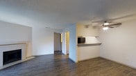 This single-floor residence in Lewisville, Texas offers an open and functional layout designed for comfortable everyday living. The main living area is finished with dark hardwood-style flooring that adds warmth and contrast against the crisp white walls, creating a clean and inviting atmosphere throughout the space.

A notable architectural feature is the pass-through kitchen counter, which connects the kitchen to the living area and promotes an open flow between the two spaces. The kitchen is equipped with a refrigerator visible through the pass-through, and the countertop ledge provides a convenient surface for casual dining or food preparation. A ceiling fan is installed in the living area, offering both practical ventilation and a subtle design element.

The textured popcorn ceilings are consistent throughout, adding a classic residential character to the interior. A hallway visible from the main living area leads to additional rooms, suggesting a well-organized floor plan that separates living and private spaces effectively. Natural light filters into the space, contributing to the overall bright and open feel of the interior. The unit presents a straightforward, move-in-ready layout suited for a range of lifestyles.