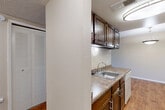 Located at 3030 E Fountain Blvd in Colorado Springs, CO, this one-bedroom, one-bathroom unit offers a practical and comfortable single-floor layout. The galley-style kitchen is outfitted with dark wood cabinetry lining both walls, laminate countertops, a double stainless steel sink, a coil-top range, and a dishwasher, all set atop warm hardwood-style flooring beneath flush-mount ceiling lighting. The kitchen opens directly into the combined dining and living area, where the transition from hardwood-style flooring to plush carpet creates a natural delineation between the two spaces. A pendant light fixture anchors the dining area, while the living room benefits from a sliding glass door that fills the space with natural light and provides direct access to a private balcony with outdoor views. The bedroom features soft carpeting, a double-door closet, and a window with blinds for adjustable light control. The bathroom includes a vanity with granite-style countertops, a round mirror with accent lighting, hardwood-style flooring, and a tiled shower surround. The unit is further complemented by three closets throughout, a utility room, and a connecting hallway, offering generous storage options. Textured ceilings are found throughout the home.
