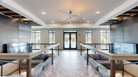 Located at 500 Congaree Rd in Greenville, South Carolina, this expansive single-floor community amenity space offers a thoughtfully designed environment built for socializing, relaxation, and productivity. The open-concept layout spans a generous footprint and is anchored by a striking central lounge area featuring herringbone-patterned tile flooring, built-in sectional seating, and a dramatic sputnik-style chandelier suspended from a coffered ceiling.

The clubhouse kitchen serves as a functional centerpiece, outfitted with a large white quartz island, stainless steel appliances including a beverage refrigerator, and bold woven pendant lighting. Adjacent to the kitchen, a live-edge wood communal dining table surrounded by blue upholstered chairs provides an inviting gathering space, complemented by an industrial-style fireplace with dark tile surround and exposed wood beam accents on the ceiling.

Throughout the space, exposed brick columns and black-framed glass partitions add a modern industrial character. Multiple seating nooks offer intimate lounging areas bathed in natural light from oversized windows overlooking lush landscaping and the surrounding community. A separate fitness center is accessible through glass double doors. The space concludes with a direct view and access to an outdoor pool area, making it a well-rounded amenity destination.