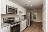 Located at 1404 Old Newport Hwy in Sevierville, Tennessee, this single-floor unit offers a clean, modern design with a cohesive aesthetic throughout. The kitchen is a standout feature, outfitted with crisp white shaker-style cabinetry, granite countertops, and a full suite of stainless steel appliances including a range, over-the-range microwave, dishwasher, and refrigerator. Recessed lighting illuminates the space efficiently, complementing the natural light that filters in through the windows. Wood-look plank flooring runs continuously throughout the unit, providing both durability and a warm, unified appearance. The open layout connects the kitchen to the living and dining areas seamlessly, creating a spacious and functional flow. A dedicated room with a dark-framed entry door offers flexible use as a bedroom or living space, benefiting from natural light through a windowed door panel. The bathroom features a full tub-shower combination, a toilet, and a vanity with granite countertop, maintaining the consistent design language found throughout the unit. Neutral wall tones in soft beige contribute to a bright, inviting atmosphere across all areas of the space.