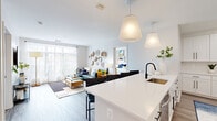 This single-floor residence is designed with a clean, contemporary aesthetic characterized by neutral tones, light wood-style flooring, and an abundance of natural light. The open-concept layout seamlessly connects the kitchen, dining, and living areas, creating a cohesive and functional shared space.

The kitchen is well-appointed with white shaker-style cabinetry, quartz countertops, stainless steel appliances, and a large island with bar seating. A matte black faucet adds a modern contrast, while pendant lighting overhead enhances the space's refined look. The kitchen flows directly into the living area, which features large windows with sheer curtains that draw in generous natural light and offer views of surrounding greenery.

Two bedrooms each include oversized windows with outdoor views, providing a bright and airy atmosphere. The primary bathroom features a double-sink vanity with white cabinetry, quartz countertops, a frameless glass walk-in shower with marble-style tile surround, and light tile flooring. The secondary bathroom offers a tub-shower combination and a single white vanity. Throughout, the space maintains a cohesive modern design with consistent finishes and a light, welcoming ambiance.